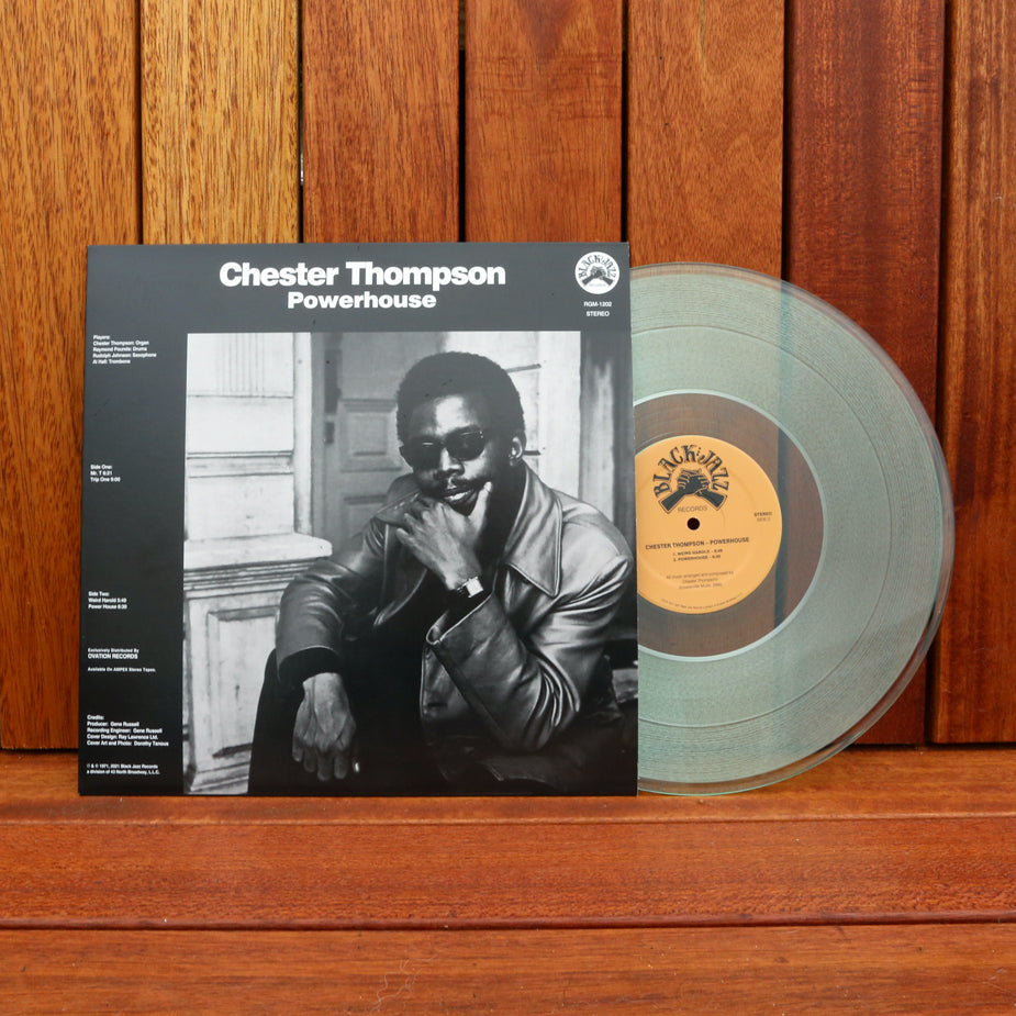 A limited clear vinyl record of "Chester Thompson - Powerhouse" by Tandem Coffee Roasters stands next to its album cover. The cover features a black-and-white photo of Chester Thompson wearing sunglasses and a leather jacket, sitting and resting his chin on his hand. The text reads "Chester Thompson - Powerhouse".