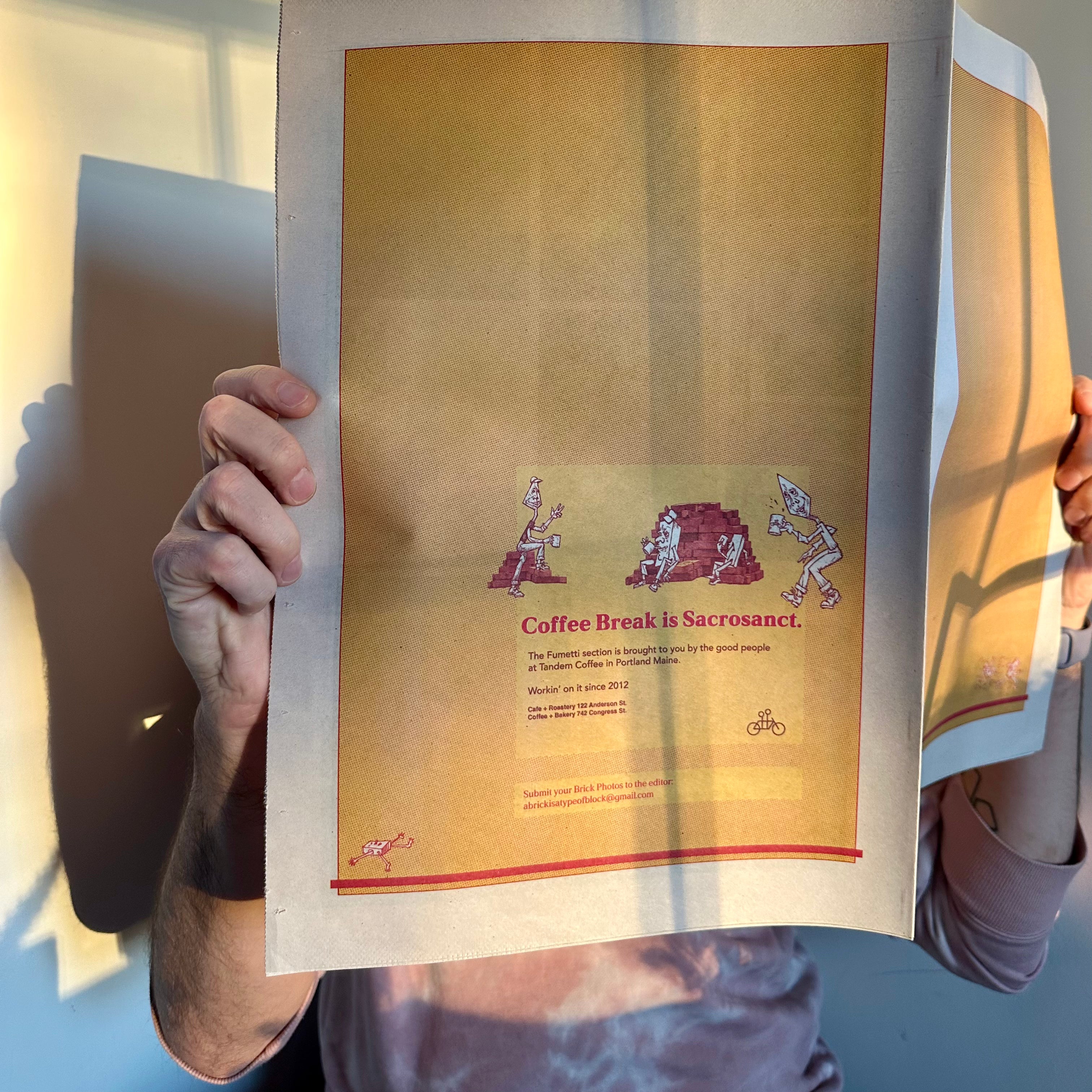 A person holds up a newspaper, obscuring their face. The page features an illustration with text that reads "Coffee Break is Sacrosanct." Just like the art of Alexis Iammarino, sunlight casts playful shadows on the wall behind. They are wearing a Brick Tee from Tandem Coffee Roasters.