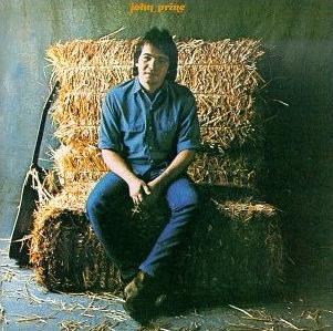 A man in a blue shirt and jeans sitting on a hay bale in front of a blue wall, holding a Tandem Coffee Roasters album, looking thoughtfully at the camera.