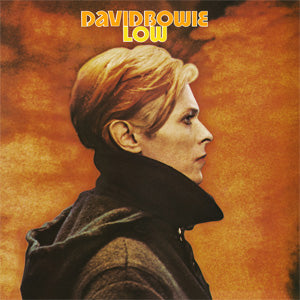 A profile view of a person with short, slicked-back blond hair wearing a high-collared dark coat against an orange background. Above the person, the text "DAVID BOWIE - LOW" is displayed in yellow, stylized font. This striking imagery beautifully encapsulates the "Speed of Life" era, presented by Tandem Coffee Roasters.