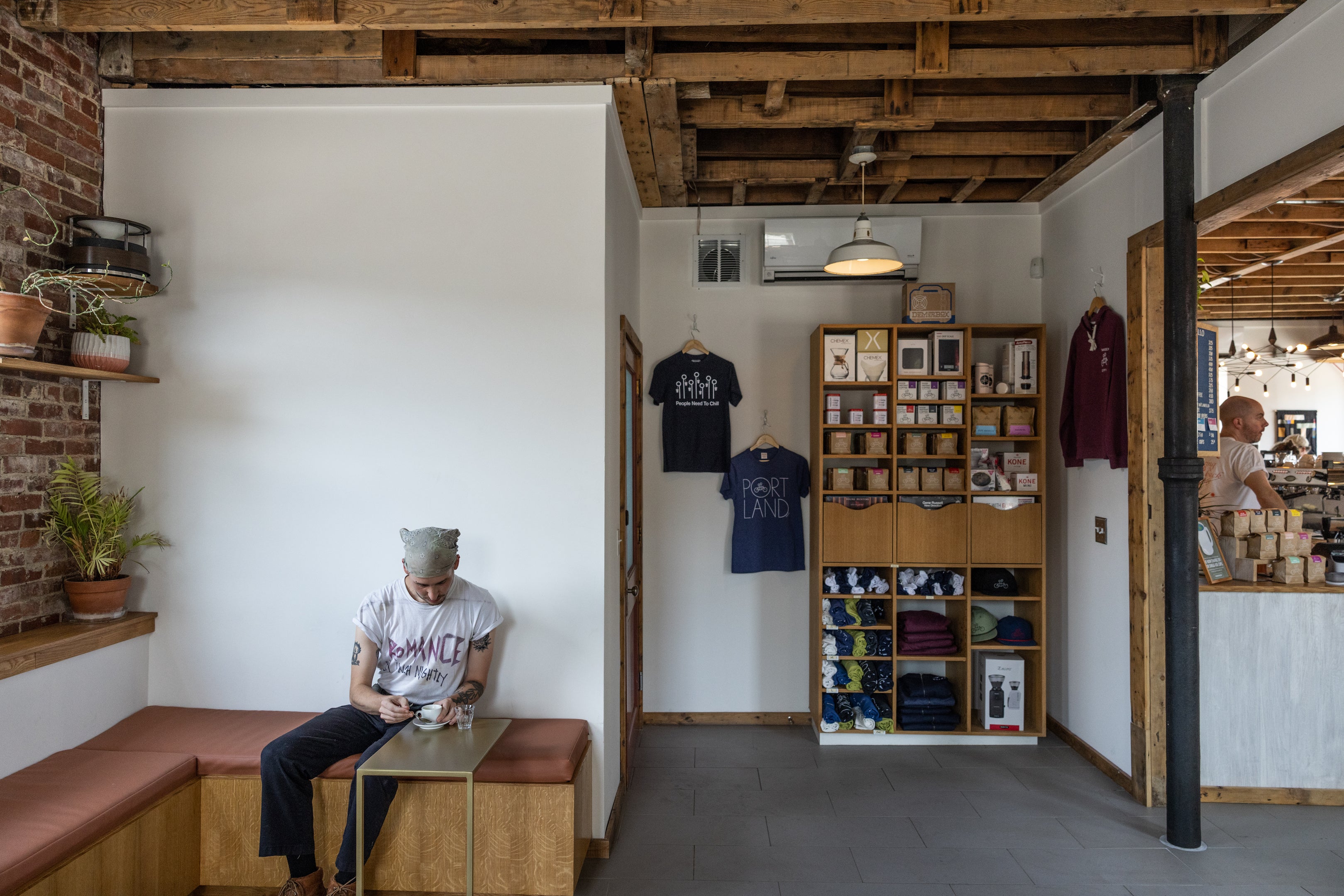 A person sits on a bench using a smartphone in a cozy café with rustic decor, including exposed beams, wooden shelves, and a variety of merchandise.