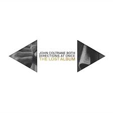 The album cover for "John Coltrane - Both Directions At Once, THE LOST ALBUM" by Tandem Coffee Roasters features the title and artist name prominently in the center, flanked by triangular shapes with partial black-and-white images. The minimalist white background accentuates the themes of "One Down, One Up.