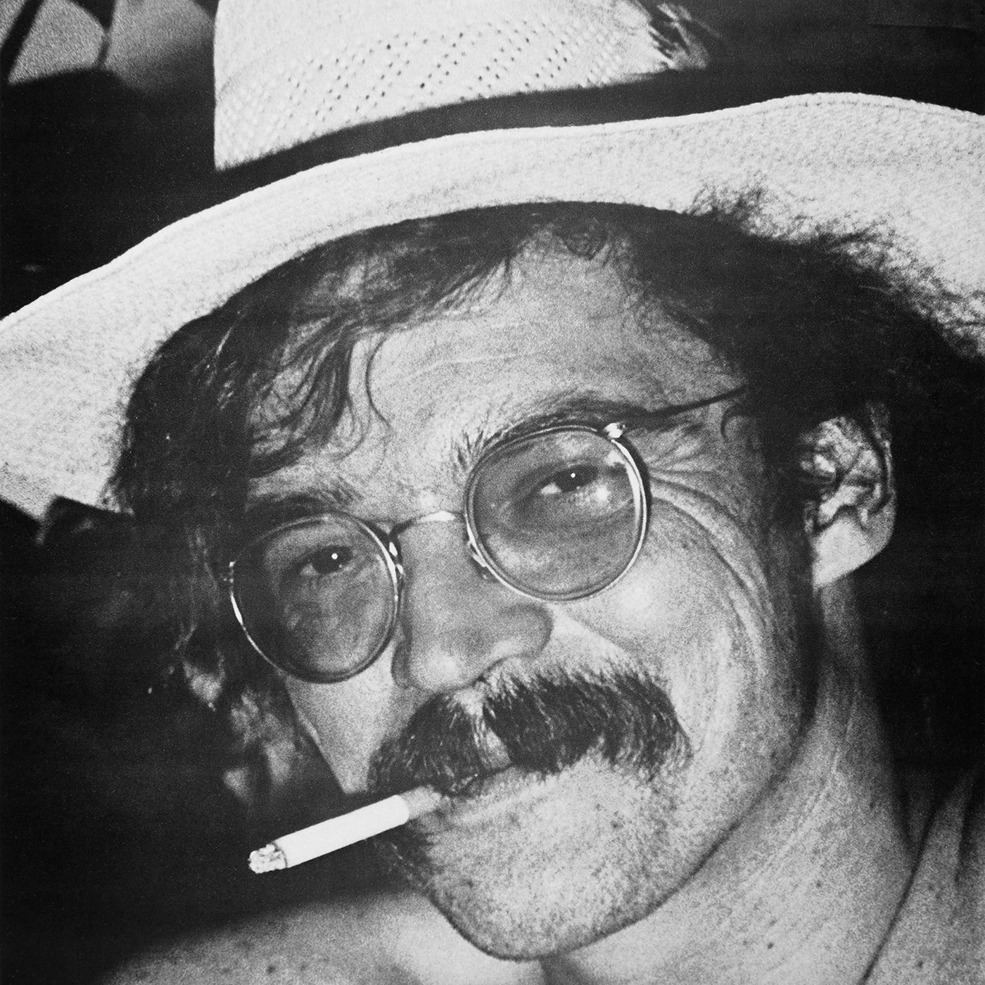 Black and white photo of a man wearing round glasses and a straw hat, with a mustache, smiling slightly with a cigarette hanging from his lips. This image serves as the iconic album cover for Tandem Coffee Roasters - Juarez